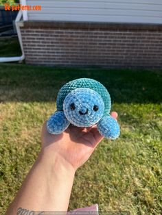 a hand holding a small stuffed animal in the grass