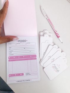 a person holding a pink piece of paper next to some tags and pens on a table