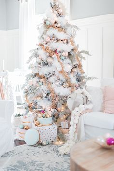 a white christmas tree in a living room with pink and blue ornaments on the top