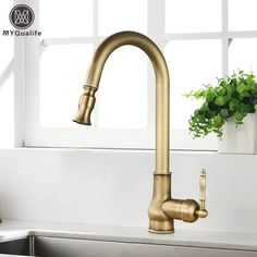 a kitchen sink with gold faucet and white counter top in front of windows