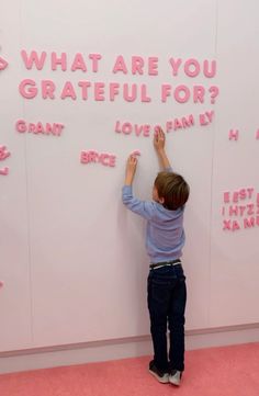 a young boy writing on a wall with pink letters and words written on it that read, what are you grateful for?