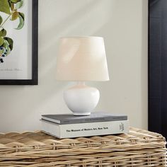 a white lamp sitting on top of a wicker table next to a framed painting