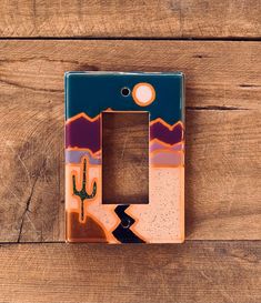 a decorative light switch plate with a cactus on the front and desert landscape painted on the back