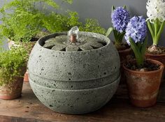 an outdoor fountain made out of concrete with water running from it's top and surrounded by potted plants