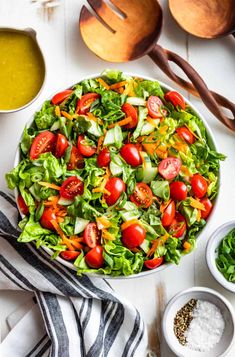 a salad with tomatoes and lettuce in a bowl next to other ingredients on a white table