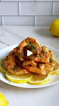 a white plate topped with shrimp and lemon wedges on top of a marble counter