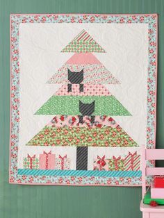 a quilted wall hanging next to a pink chair and green wall with a cat on it