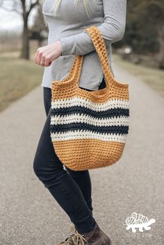 a woman is holding a crocheted bag in her hand while standing on the road