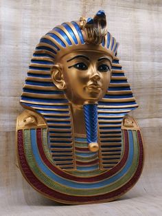 an egyptian mask made out of gold, blue and red strips with a crown on top