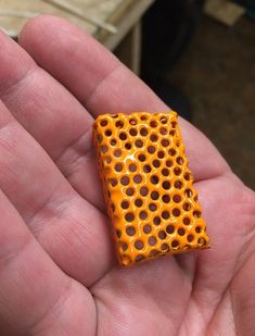 a hand holding a small orange object in it's left hand, with holes on the surface