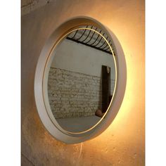 a round mirror hanging on the wall next to a brick wall with a light underneath it