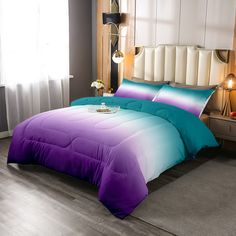 a bed with purple and blue comforters in a room next to a lamp on a table