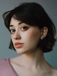 a painting of a woman with dark hair and blue eyes, wearing a pink shirt