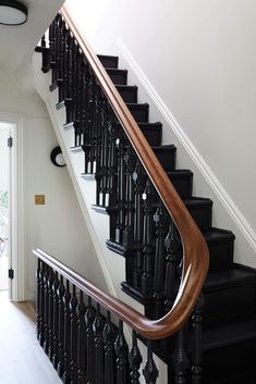 a staircase with black railing and wooden handrails in front of a white door