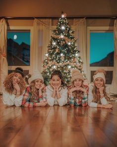 four girls are posing in front of a christmas tree with their hands on their cheeks