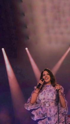 a woman standing in front of three spotlights holding a microphone and singing on stage