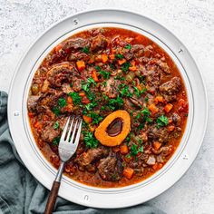 a white plate topped with meat and carrots next to a fork on top of a table