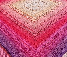 a crocheted blanket is sitting on top of a bed with pink, purple and yellow colors