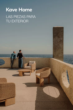 two people standing on the edge of a balcony overlooking the ocean with chairs and couches