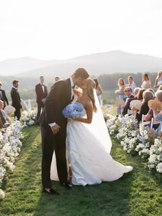 a bride and groom kissing in front of an outdoor ceremony with white flowers on the grass