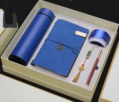 an open box containing a blue notebook, pen, and keychain with other items in it