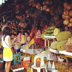 a woman standing in front of a fruit stand filled with lots of fruits and vegetables