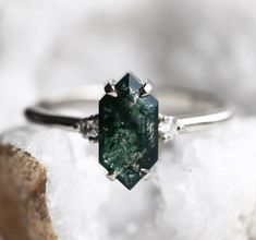 a green diamond ring sitting on top of a rock