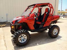 a red and black four passenger vehicle parked in front of a white building with large tires