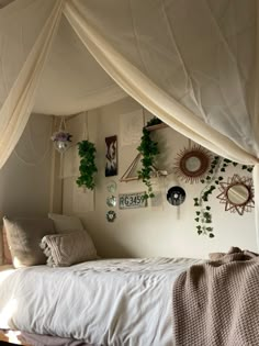 a canopy bed with white sheets and plants hanging on the wall next to it in a bedroom