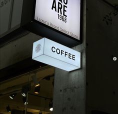 a coffee shop sign hanging from the side of a building at night with lights on