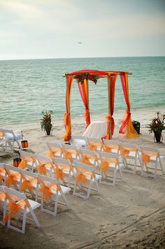 an orange and white wedding set up on the beach