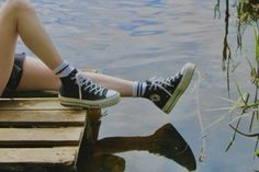 a person is sitting on a dock with their feet in the water and wearing tennis shoes