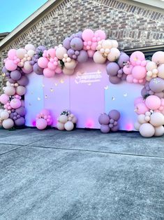 a balloon arch in front of a house with pink and purple balloons hanging from it