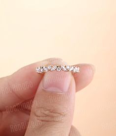 a woman's hand holding a ring with five diamonds on it, in front of a pink background