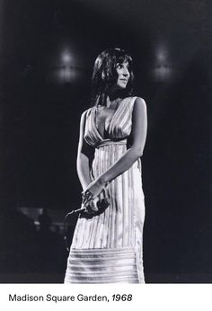 a black and white photo of a woman in a dress holding a microphone on stage