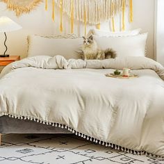 a cat sitting on top of a white bed in a room with fringes hanging from the ceiling