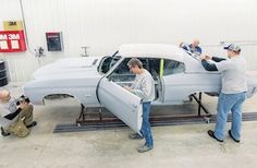 two men working on a car in a garage with another man standing next to it