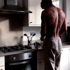 a shirtless man standing in front of a stove top oven next to an oven