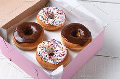 four donuts with chocolate frosting and sprinkles in a pink box