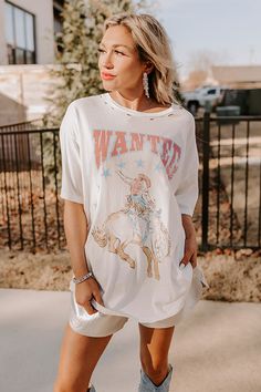 - Saddle up and put on your best boots with this trendy tee! - Unlined lightweight material with subtle distressed detail - A blue, brown, and pink hued 'WANTED' cowboy graphic design - A relaxed silhouette that ends in a straight Measurements S : Bust 42", Hip 44", Length 27.5", Sleeve Length 7.5", Waist 42". M : Bust 46", Hip 48", Length 28.5", Sleeve Length 8", Waist 46". L : Bust 48", Hip 50", Length 29", Sleeve Length 8", Waist 48".