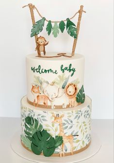 a three tiered cake decorated with jungle animals and palm trees, the words welcome baby written on top