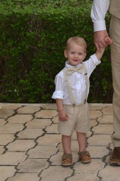 a little boy in a bow tie and suspenders holding his father's hand