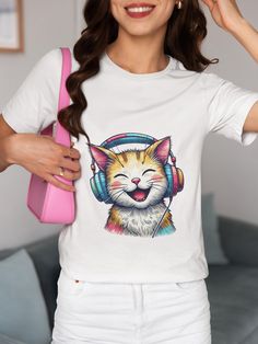 This unisex T-shirt features an adorable orange and white cat joyfully wearing oversized colorful headphones, perfect for both music enthusiasts and cat lovers. The vibrant, playful design makes this shirt a great addition to your casual wardrobe or as a unique gift for friends and family. Made with high-quality materials, it provides both comfort and style for any occasion. Express your love for music and felines in one fun graphic tee! We utilize the authentic Bella Canvas 3001 brand, renowned for its UNISEX design, making it one of the most sought-after shirts in the market. Prior to placing an order, kindly refer to our size chart. It can be located in both the listing's images and description. This cozy T-shirt serves as an ideal present, suitable for occasions such as birthdays, Chri Trendy White T-shirt With Cat Print, White Cat Design T-shirt For Summer, White Summer T-shirt With Cat Design, White Cat Design T-shirt For Streetwear, White T-shirt With Cat Design For Streetwear, Cat With Headphones, Orange And White Cat, Smiling Cat, Cool Graphic Tees