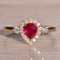 Rue Saint-Rustique: Vivid Pear Shaped Natural Ruby And Natural Diamond Ring. This Exquisite Piece Centers On A Dazzling 0.62 Carat Pear Brilliant Cut Natural Ruby, Boasting A Medium Very Slightly Purplish-Red Color Strong In Saturation, Capturing Attention With Its Vivid Allure. Surrounding The Center Is A Halo Of Round Brilliant Cut Natural Diamonds, Adding A Touch Of Brilliance And Elegance To The Design. Completing The Look Is A Single Larger Round Brilliant Cut Natural Diamond That Tops The Tapered Shank, Elevating Its Charm And Sophistication. Crafted With Meticulous Attention To Detail In 14 Karat Yellow Gold, This Ring Is Currently A Finger Size 6.5, With The Flexibility To Be Adjuste Natural Diamond Ring, Natural Ruby, Womens Jewelry Rings, Pear Shaped, Round Brilliant, Pink Yellow, Red Color, Natural Diamonds, Halo