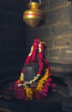 a small shrine with flowers on the ground and a pot hanging from it's side