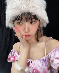 a woman wearing a white furry hat with her hand on her chin and looking at the camera