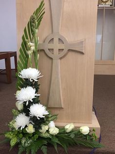 a wooden cross with white flowers and greenery in front of it on the floor