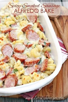 a white dish filled with pasta covered in sausage and sauce, next to a green sign that says spicy smoked sausage alfredo bakes