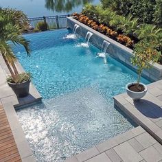 an outdoor swimming pool surrounded by plants and water features a waterfall that runs down the side of it