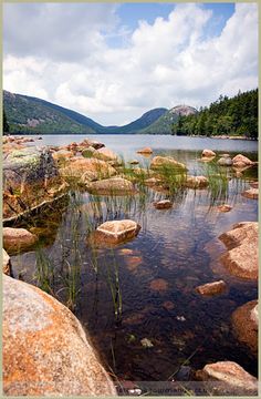 a lake surrounded by rocks and grass with mountains in the background